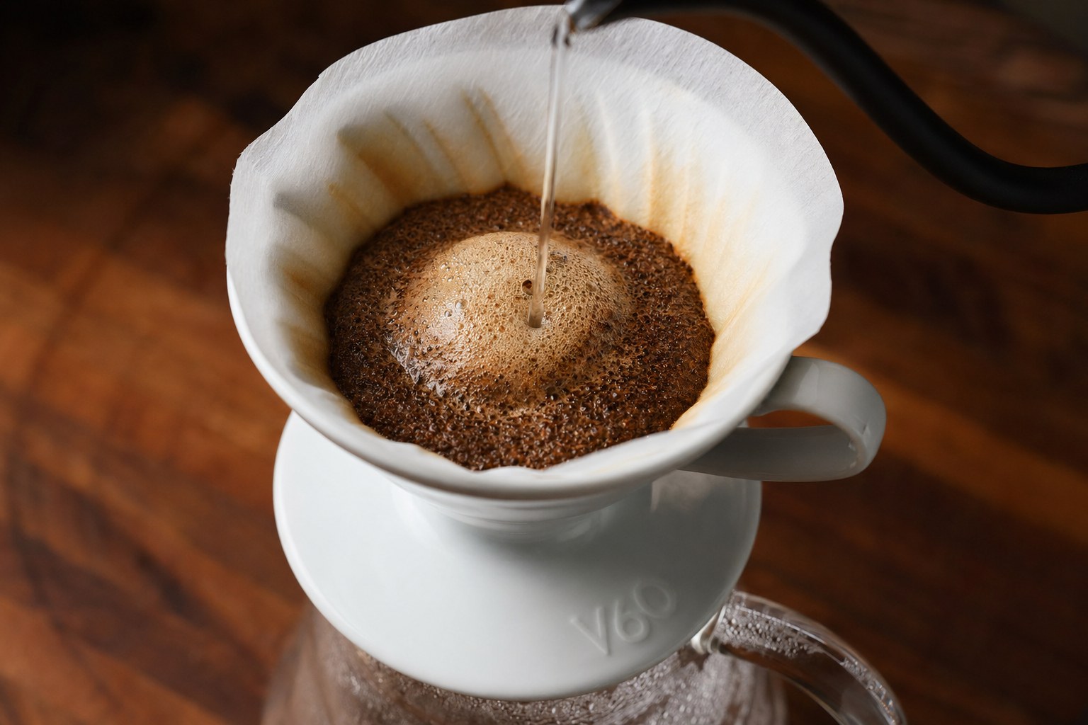 Coffee blooming inside a Hario V60 02 with a gooseneck kettle pouring hot water onto the bed